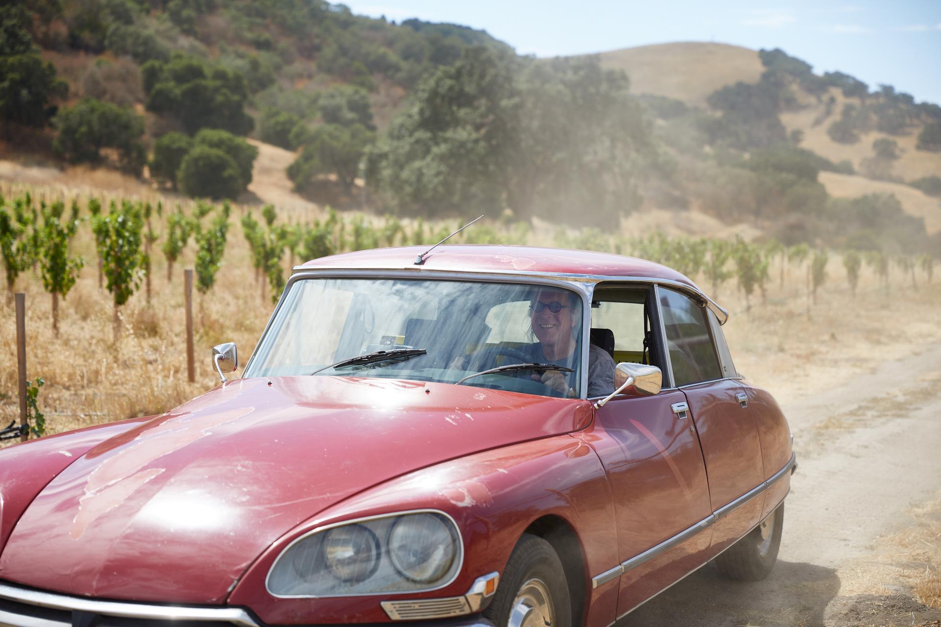 Winemaker Randall Grahm driving through a vineyard in a red car